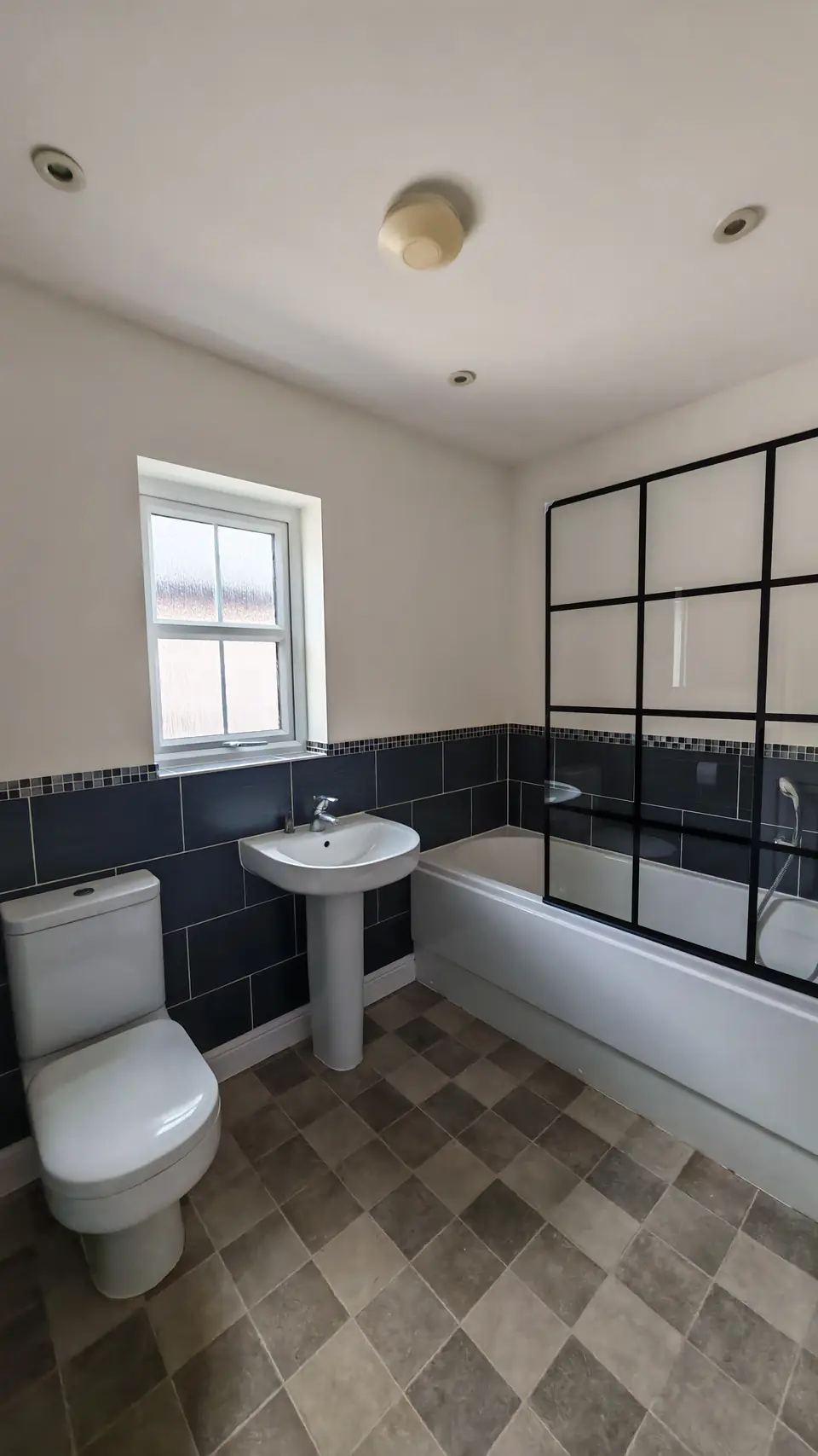 Bathroom with navy tiles to dado height, a black-framed bath screen and patterned floor