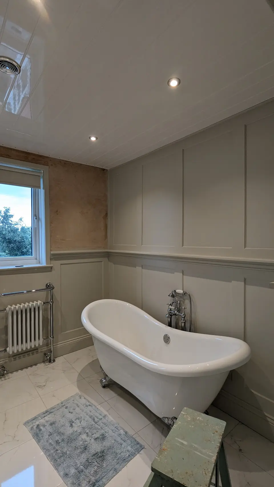 Bathroom with tree mural above sage panelling and roll-top bath
