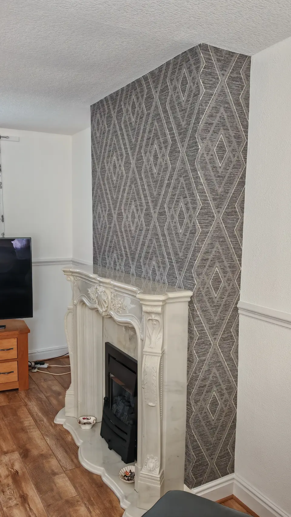 Chimney breast feature wall in a diamond-pattern wallpaper behind a marble fireplace
