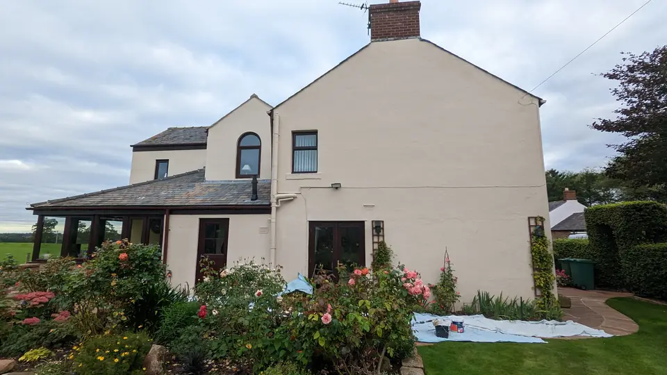 Cream-painted detached cottage with a conservatory and a flower-filled garden, after exterior painting