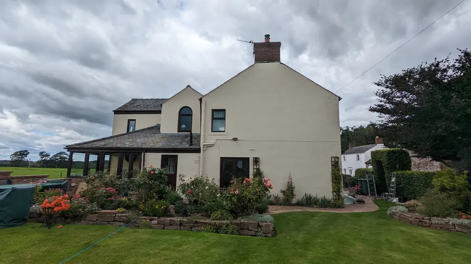 Freshly painted cream cottage seen across the lawn, with white windows and a garden room