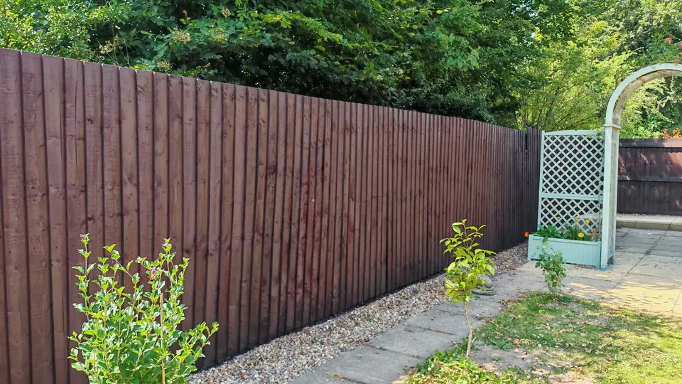 Dark brown fence alongside a garden arch and path