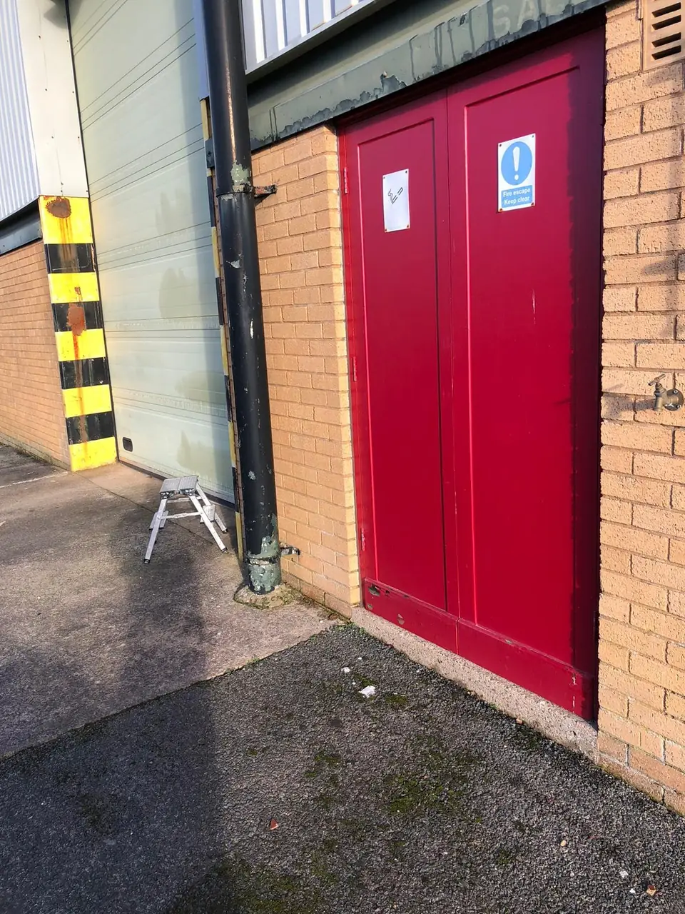 Before: faded red double fire exit doors on a commercial unit
