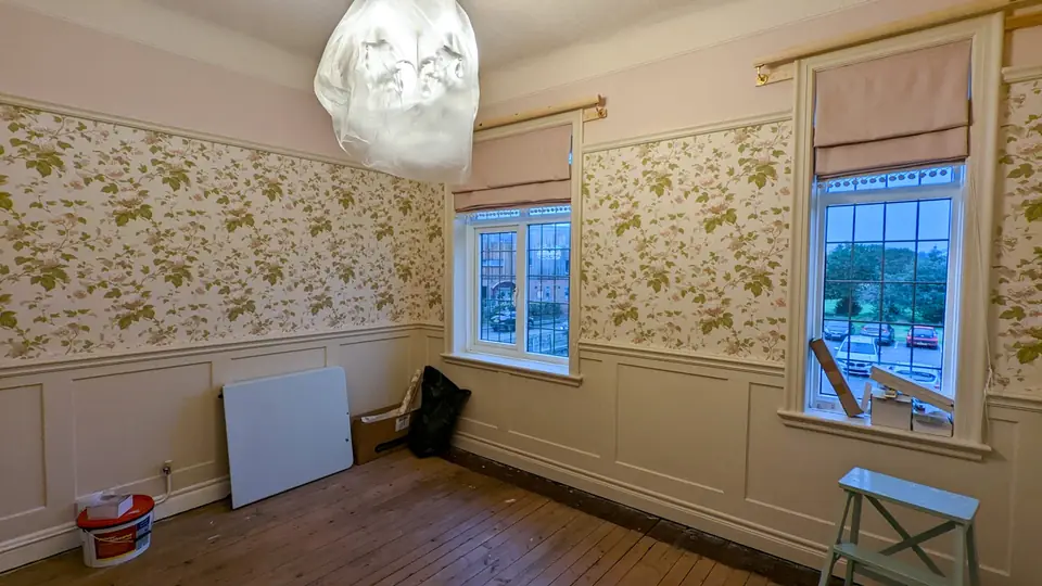 Floral wallpaper above white wall panelling in a bay-windowed room