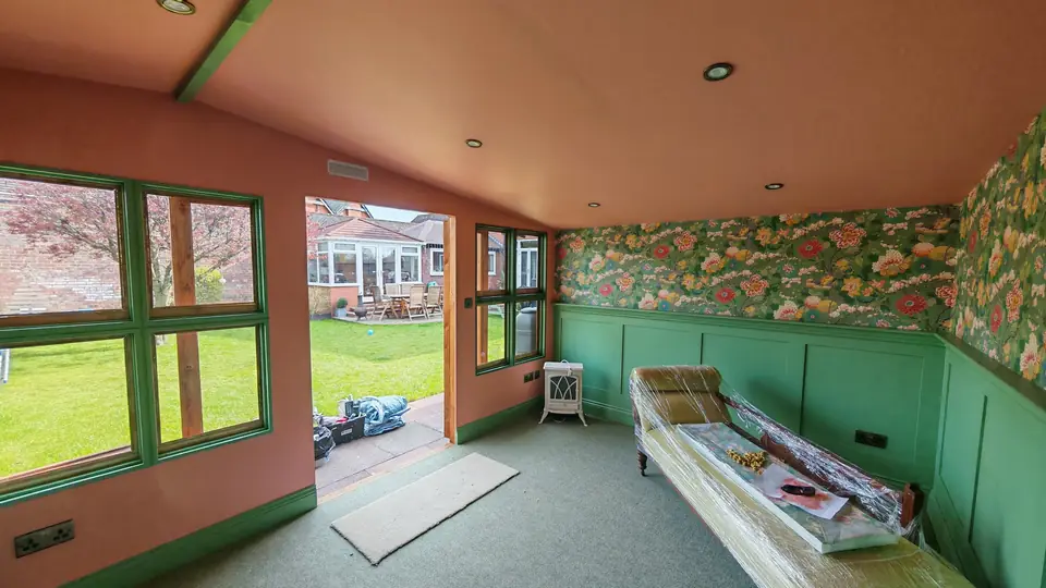 Garden room with sage green panelling, floral wallpaper and terracotta ceiling