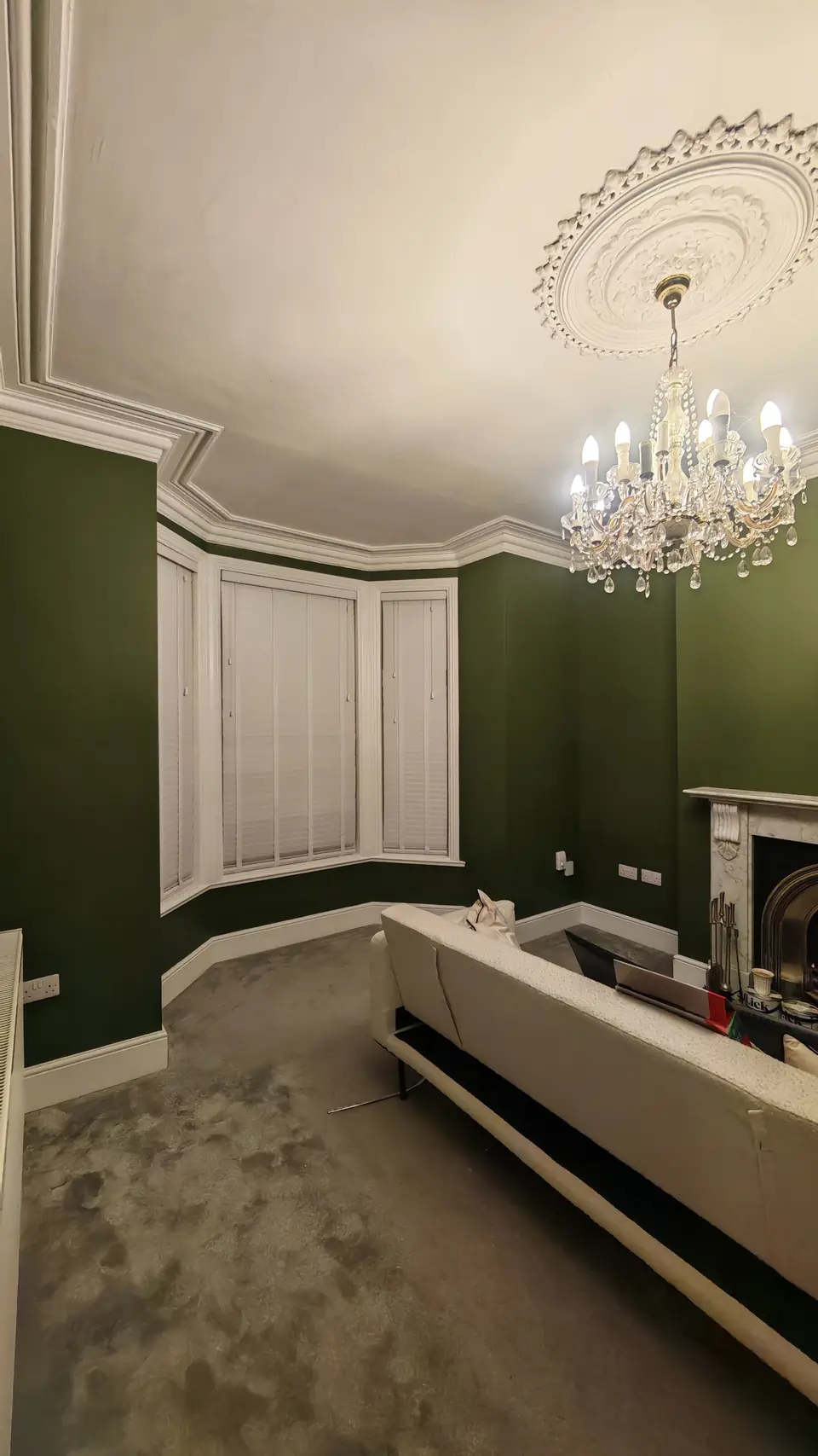 After: deep green living room with white bay shutters and chandelier