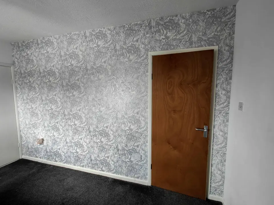 Grey and white leaf-pattern wallpaper hung around an oak door