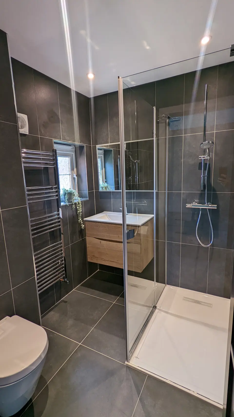 Shower room with large grey wall and floor tiles, glass walk-in screen and floating vanity