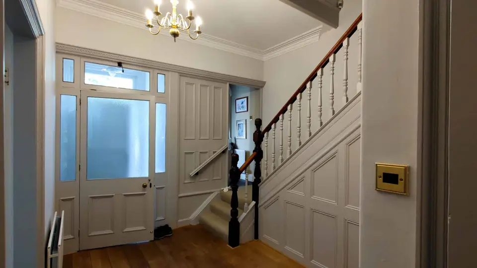 Bright hallway and staircase with white panelled walls and chandelier, decorated by A&B Decorators in Carlisle