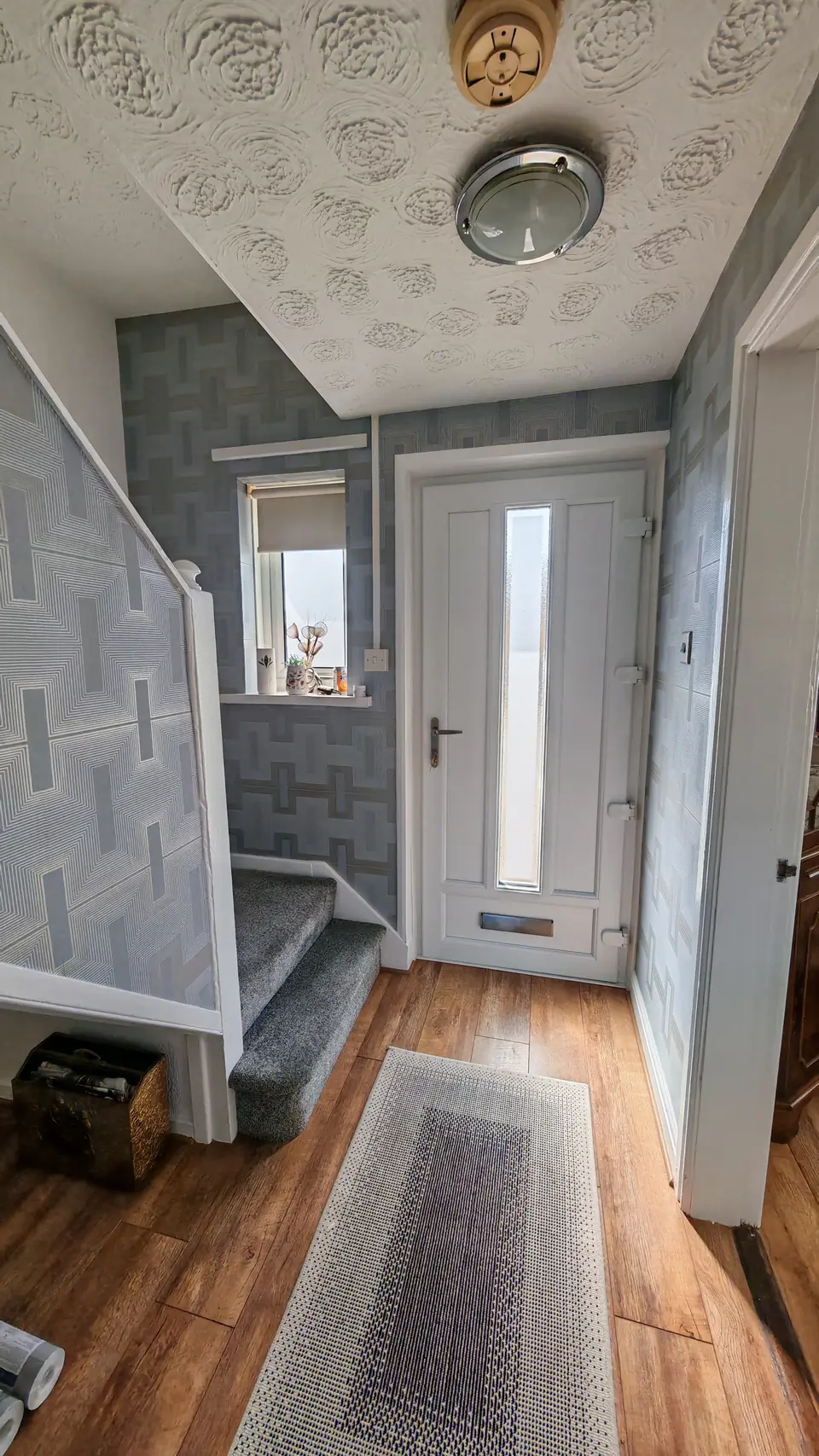 Hallway hung in a geometric grey and silver wallpaper, looking to the front door