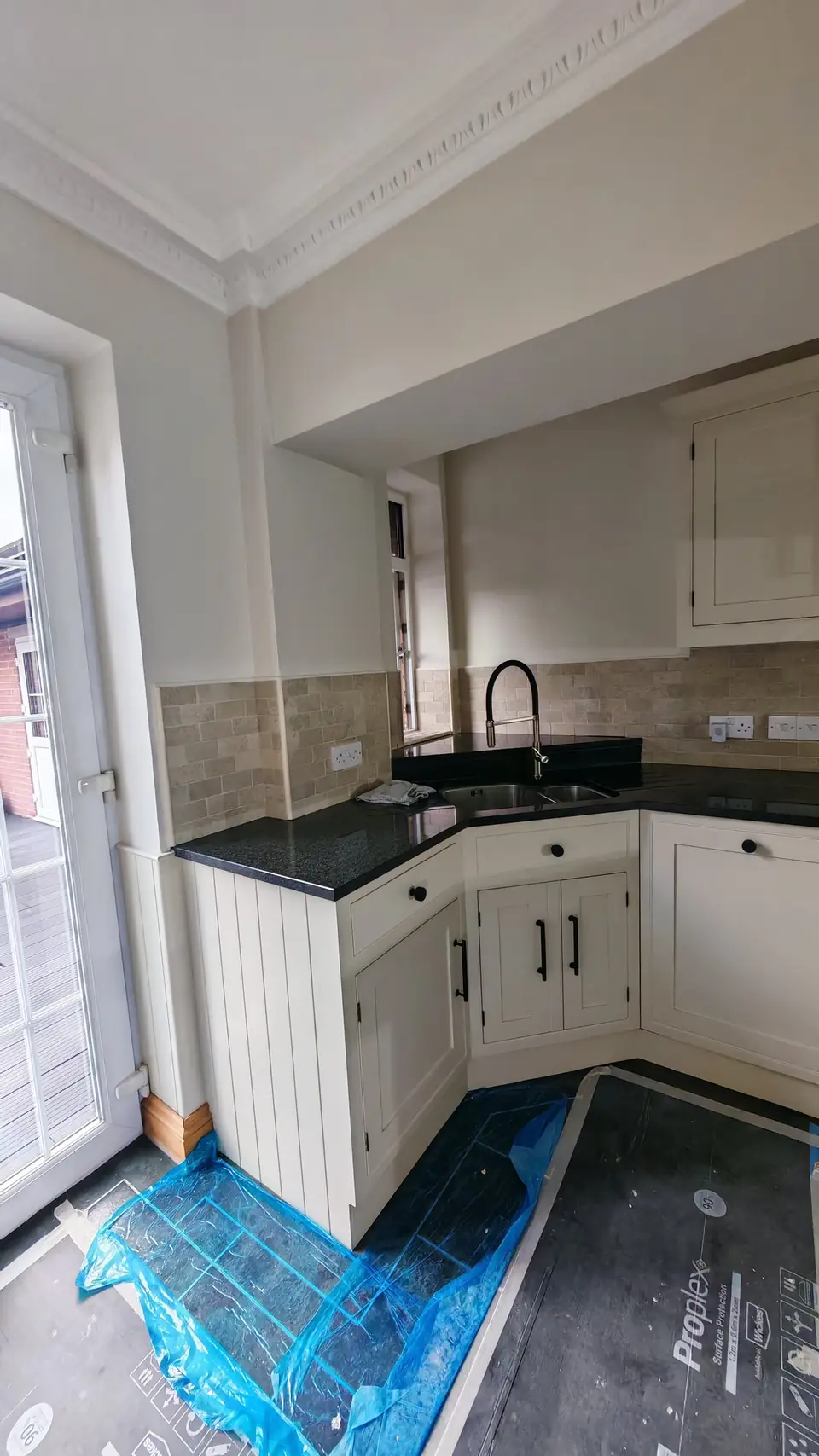 Kitchen respray: cream units and black granite worktop around the sink corner