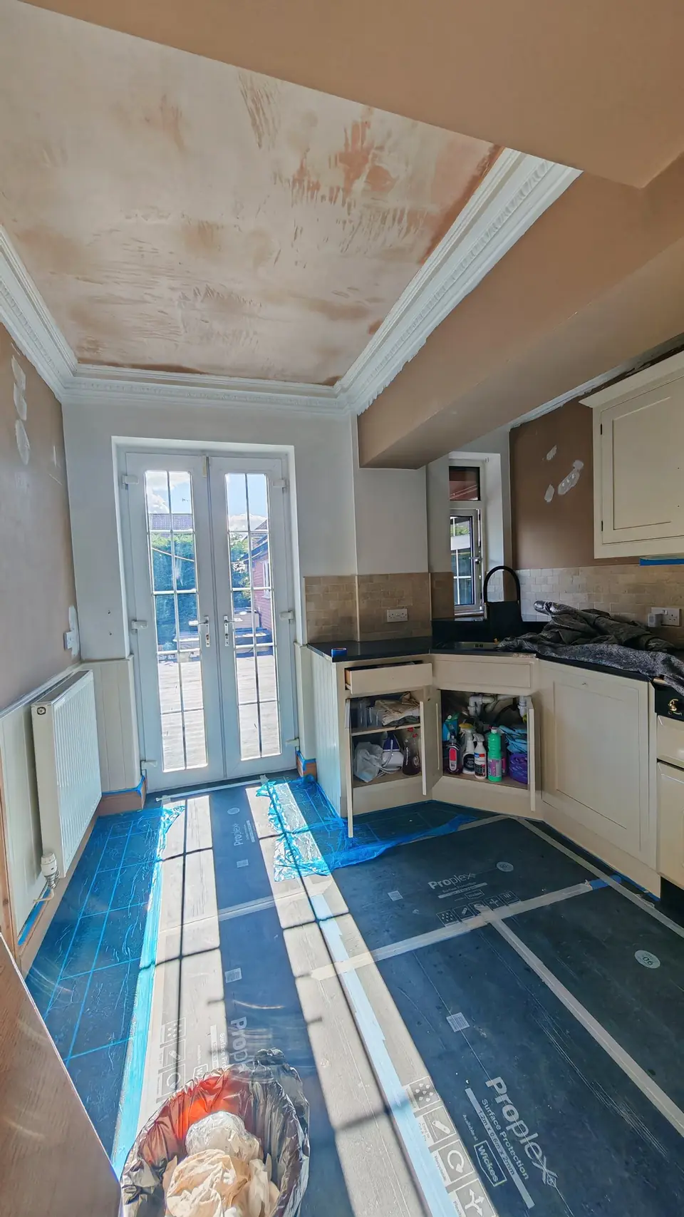 During: the kitchen mid-job, ceiling still bare plaster, walls in the old beige, worktops covered and floor protected