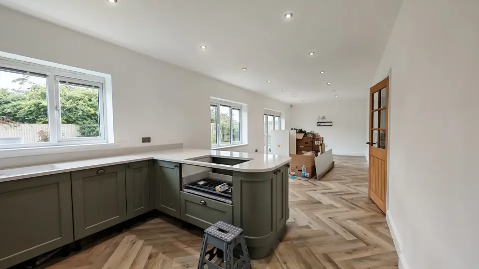 Wide view of herringbone LVT flooring in a green shaker kitchen