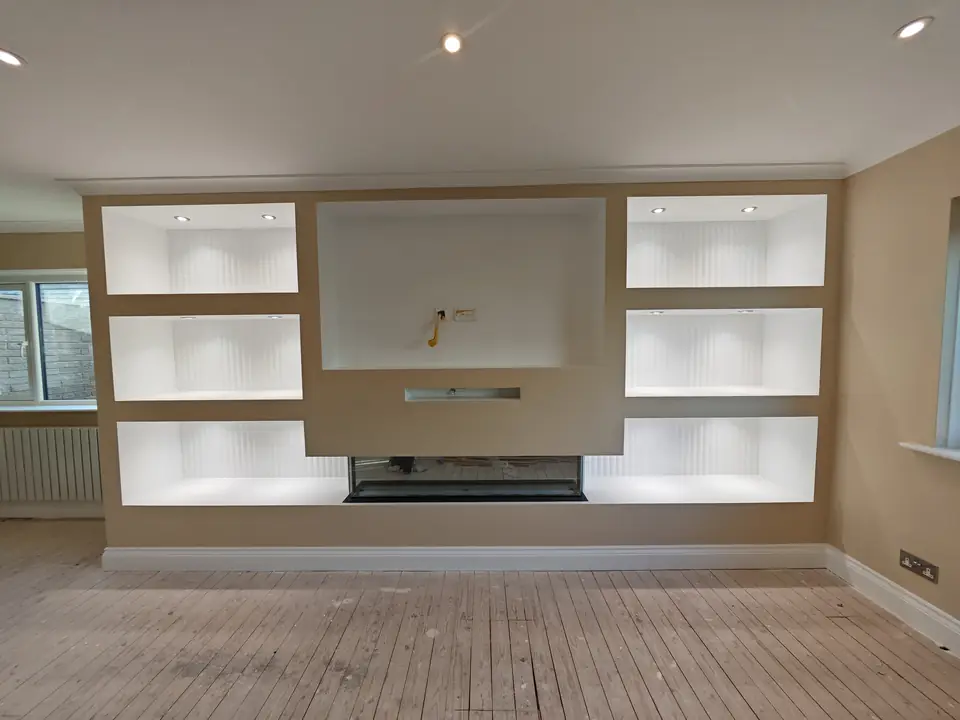 Built-in media wall with lit shelving, painted and finished in a modern living room