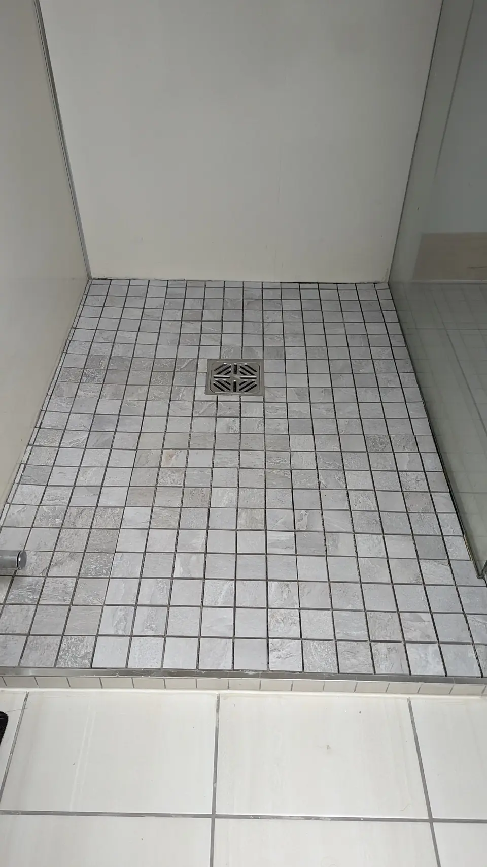 Walk-in shower floor laid in small grey mosaic tiles with a centre drain