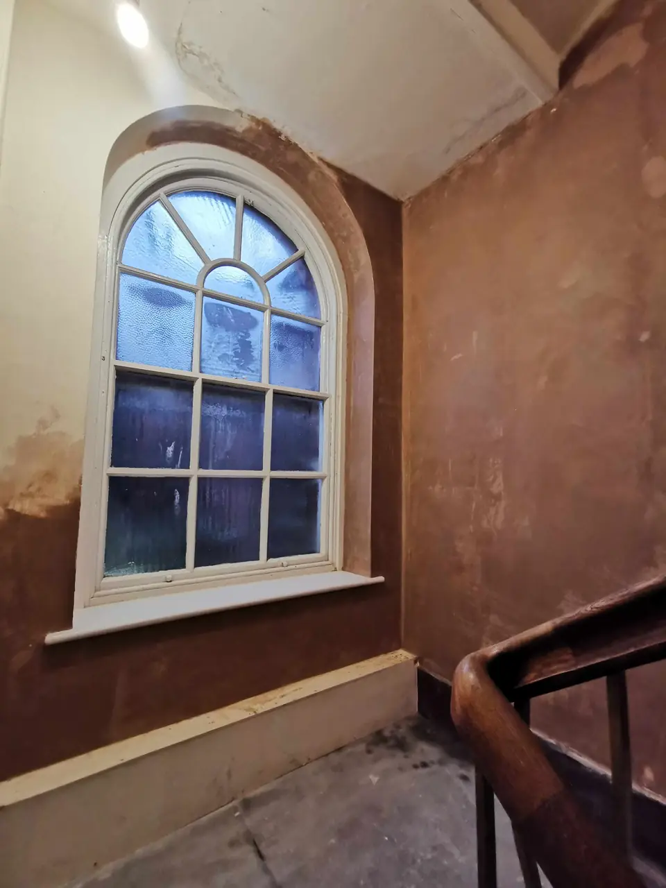 Newly plastered stairwell around an arched window, ready for a mist coat