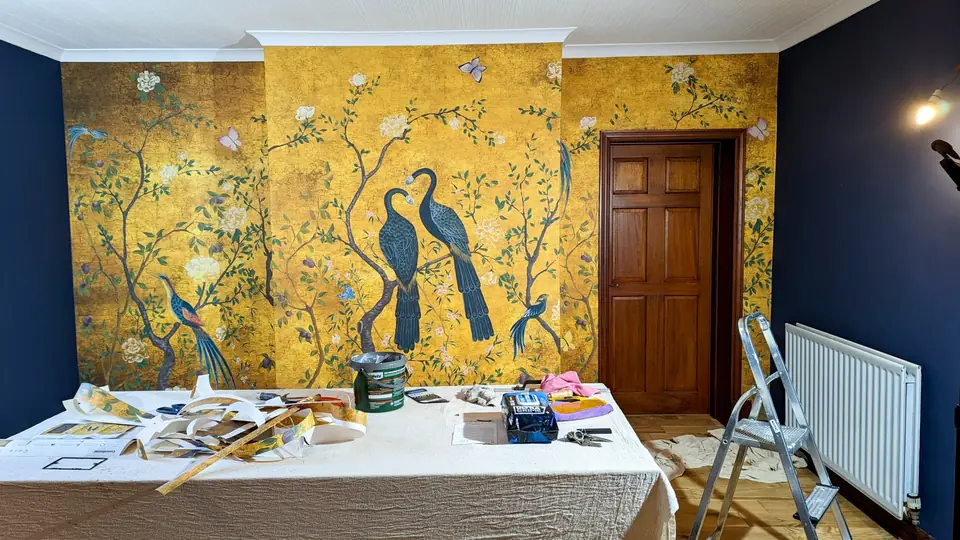Gold peacock feature wallpaper hung alongside a navy painted wall
