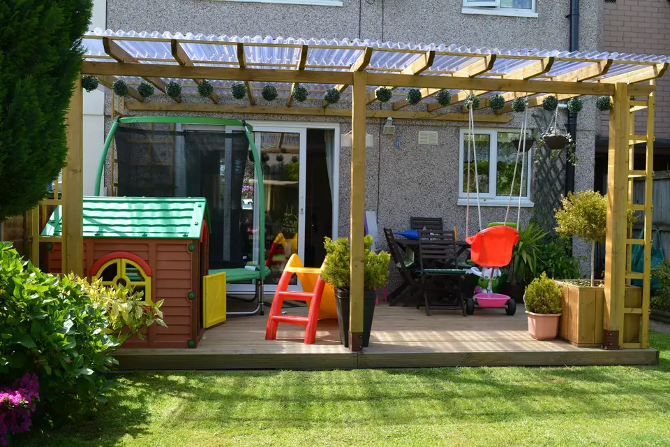 Timber pergola over a patio with a polycarbonate roof, built in a family garden