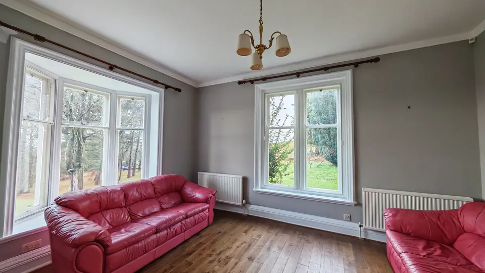 Period living room painted soft grey with white bay windows and red leather sofas