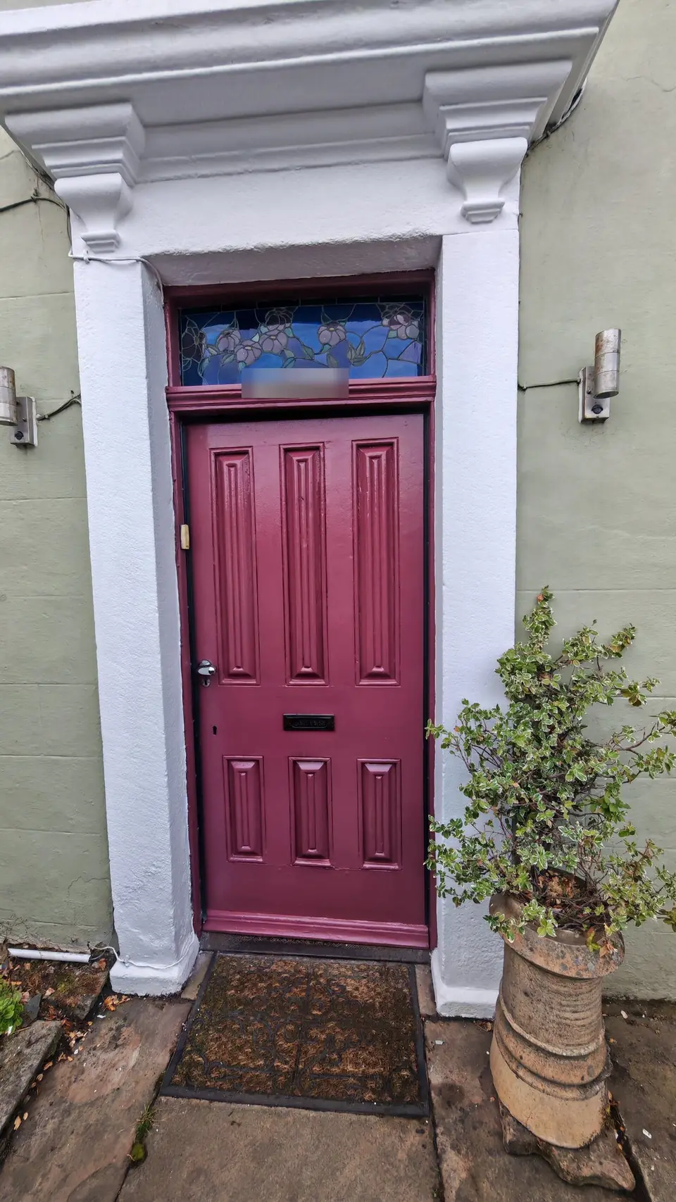 After: burgundy front door under the white stone canopy with corbels
