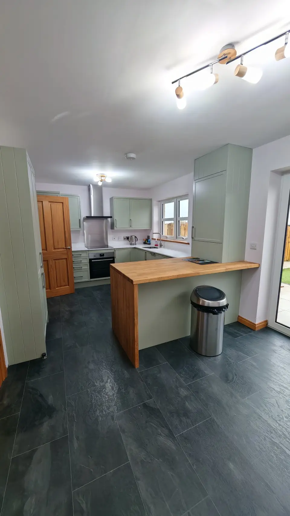 Sage green shaker kitchen with oak breakfast bar and dark slate-effect floor