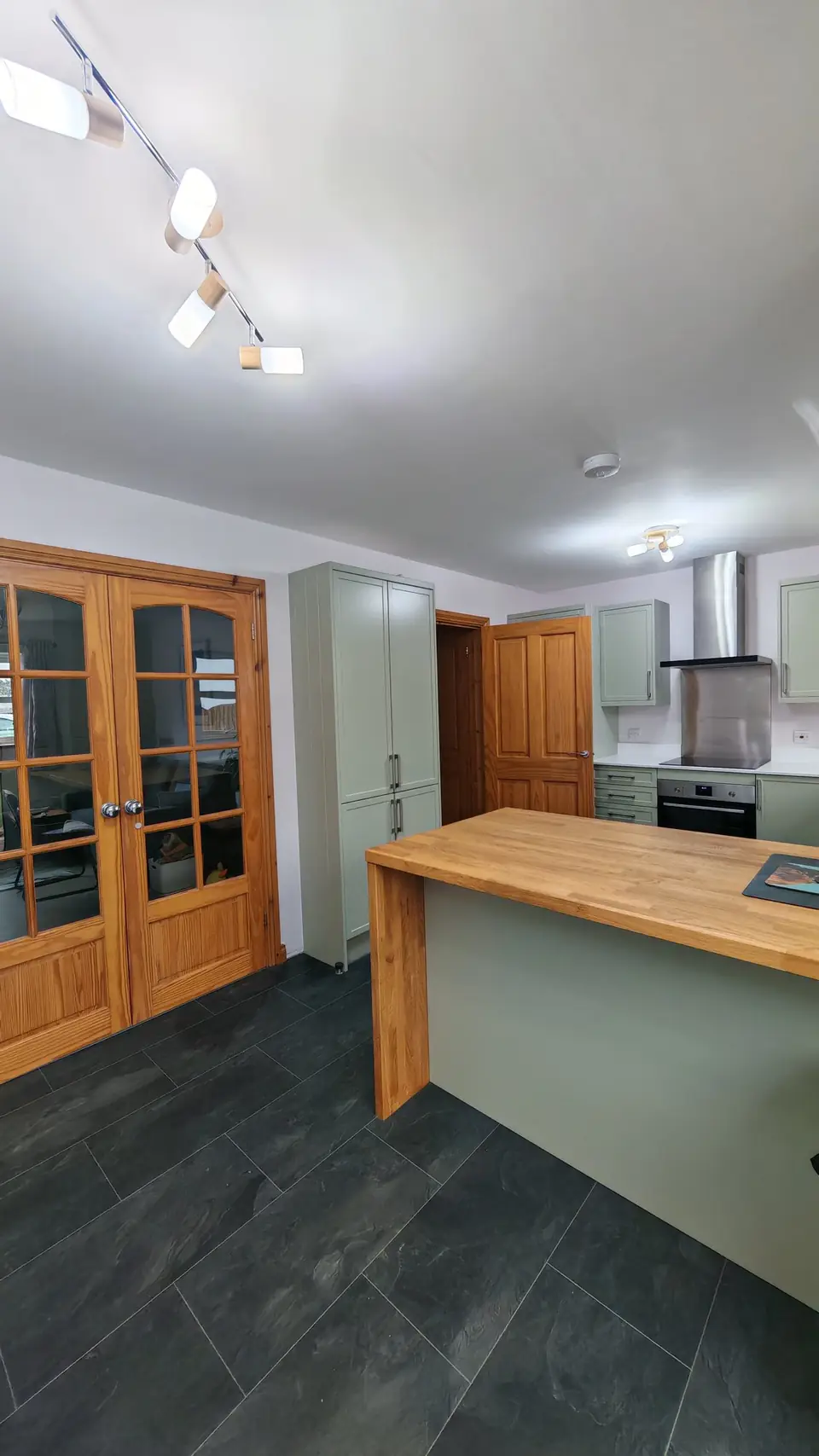 Sage green tall units and oak breakfast bar beside glazed wooden doors