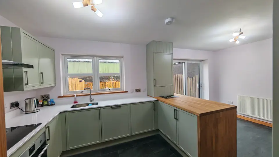 Kitchen and hallway decoration: sage green shaker kitchen with oak breakfast bar, white worktops and lilac walls