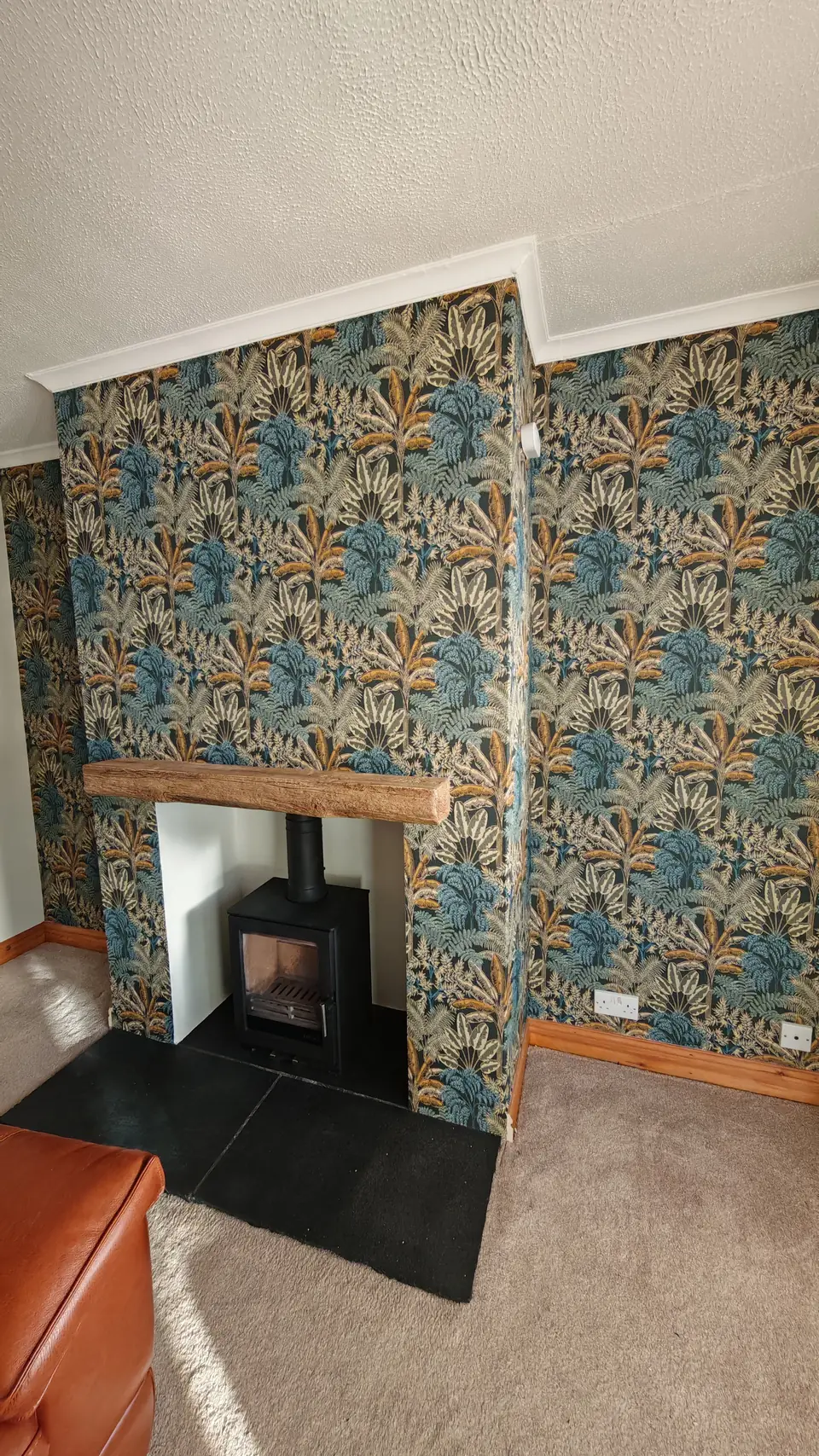 Tropical print wallpaper on the chimney breast around a woodburner