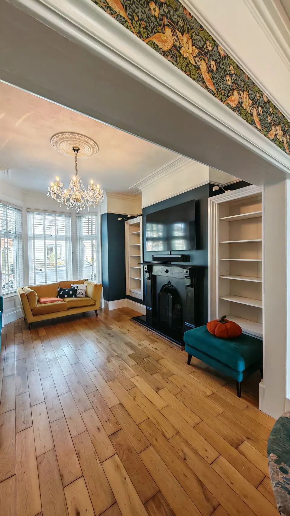 Through the arch to the bay: deep teal walls and white alcove shelving